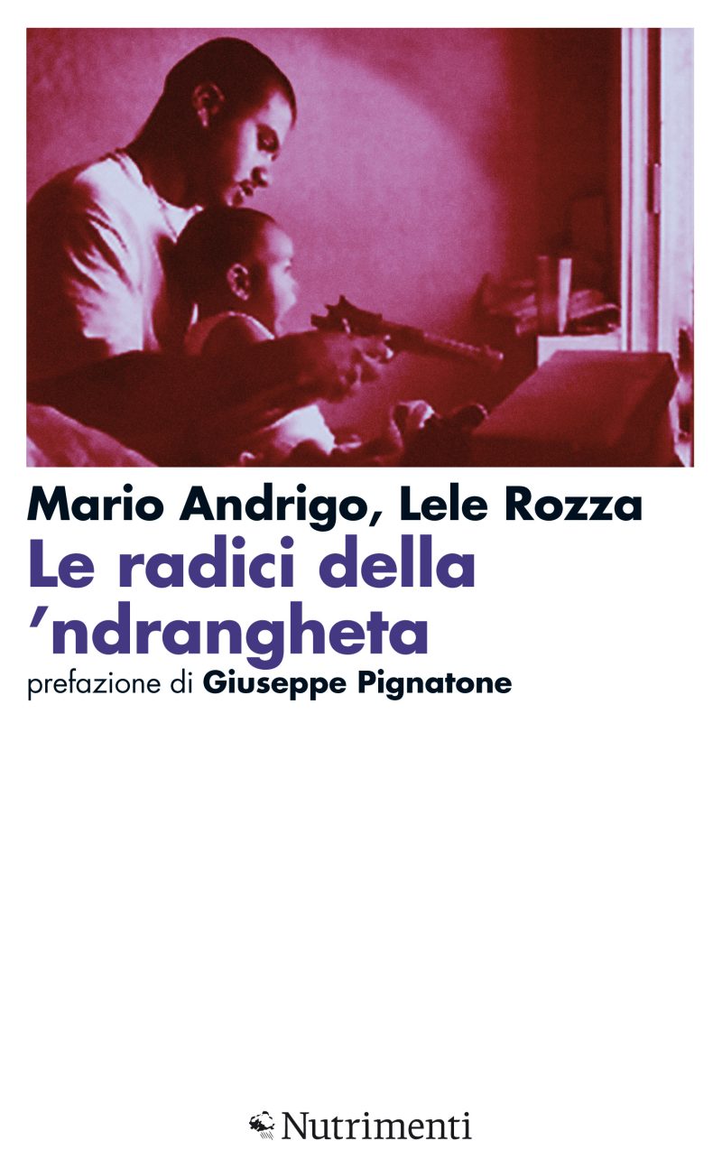 In copertina giovane padre tiene in braccio il figli di pochi mesi imbracciando una pistola